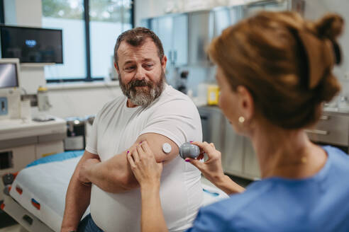 Ein Arzt bringt einen Sensor zur kontinuierlichen Überwachung des Blutzuckerspiegels am Arm eines Patienten an. Ein übergewichtiger oder fettleibiger Mann hat ein erhöhtes Risiko, an Typ-2-Diabetes zu erkranken. Konzept der Gesundheitsrisiken von Übergewicht und Fettleibigkeit. - HPIF31476