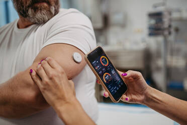 Der Arzt verbindet das kontinuierliche Glukosemessgerät des Patienten mit dem Smartphone, um den Blutzuckerspiegel in Echtzeit zu überprüfen. Ein übergewichtiger Mann ist gefährdet, an Typ-2-Diabetes zu erkranken. Konzept der Gesundheitsrisiken von Übergewicht und Adipositas. - HPIF31478