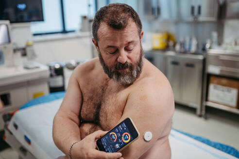 Ein Patient verbindet ein kontinuierliches Glukosemessgerät mit seinem Smartphone, um seinen Blutzuckerspiegel in Echtzeit zu überprüfen. Ein übergewichtiger Mann hat ein hohes Risiko, an Typ-2-Diabetes zu erkranken. Konzept der Gesundheitsrisiken von Übergewicht und Adipositas. - HPIF31481