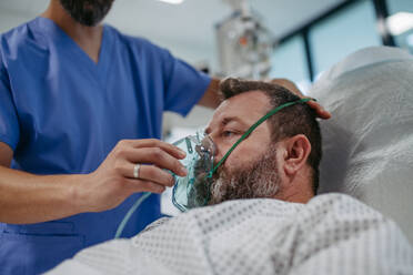 Krankenschwester passt einem Patienten im Krankenhausbett eine Sauerstoffmaske an. Mann auf der Intensivstation im Krankenhaus. - HPIF31484