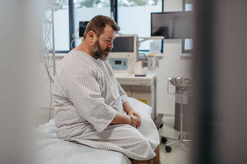 Übergewichtiger Patient im Krankenhauskittel, der auf die ärztliche Untersuchung, die Testergebnisse im Krankenhaus wartet, sich ängstlich und besorgt fühlt, Schwindelgefühle hat und starke Schmerzen hat. - HPIF31492