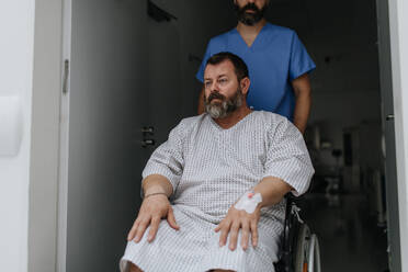 Male nurse pushing a patient in wheelchair along a hospital corridor. Overweight patient feeling anxious and has health concerns. - HPIF31501