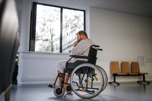 Seitenansicht des Mannes im Rollstuhl. Übergewichtiger Patient im Krankenhauskittel wartet auf eine medizinische Untersuchung im Krankenhaus. - HPIF31508