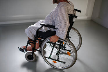 Seitenansicht des Mannes im Rollstuhl. Übergewichtiger Patient im Krankenhauskittel wartet auf eine medizinische Untersuchung im Krankenhaus. - HPIF31509
