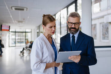 Pharmaceutical sales representative talking with the female doctor in medical building. Hospital director consulting with healthcare staff. - HPIF31521