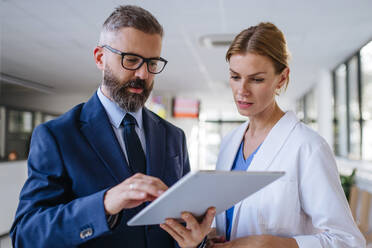 Pharmaceutical sales representative talking with the female doctor in medical building. Hospital director consulting with healthcare staff. - HPIF31526