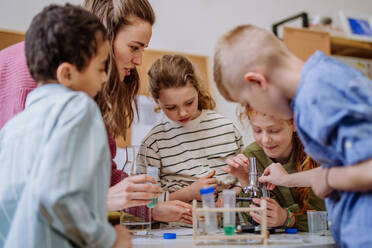 Young teacher doing chemistry experiment with her pupils during science education. - HPIF31549