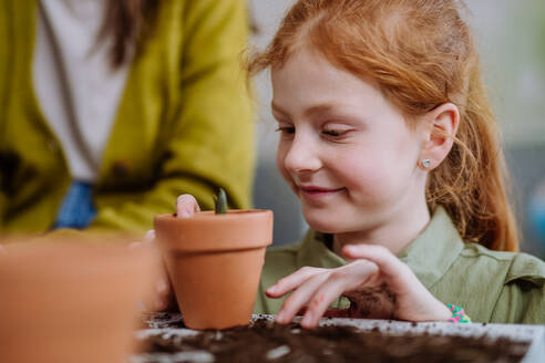 Glückliches kleines Mädchen betrachtet eine wachsende Pflanze in einem Keramiktopf. - HPIF31563