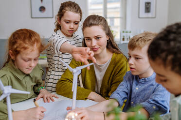 Young teacher with model of wind turbine learning her pupils about wind energy. - HPIF31584