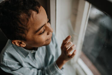Kleiner multirassischer Junge schaut aus dem Fenster. - HPIF31590