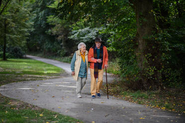 Glückliches älteres Paar in Herbstkleidung, das zusammen im Park spazieren geht. - HPIF31620