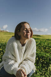 Lächelnde Frau mit geschlossenen Augen in einem Strickpullover an einem sonnigen Tag - DMGF01123