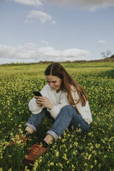 Frau mit Smartphone im Gras sitzend auf einer Wiese - DMGF01128