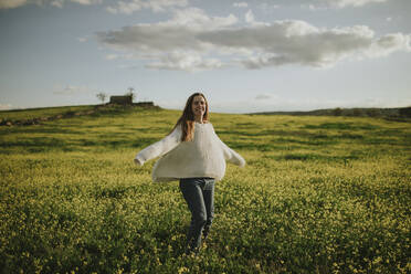 Glückliche Frau tanzt auf Gras unter bewölktem Himmel - DMGF01131