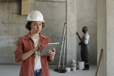 Young engineer using tablet PC with coworker in background at construction site - DSHF01328