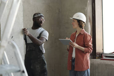 Smiling engineer holding tablet PC and having discussion with colleague at site - DSHF01334