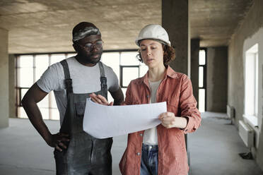Engineer having discussion over blueprint with construction worker at site - DSHF01339