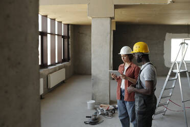 Ingenieur mit Tablet-PC und Planung mit einem Mitarbeiter auf der Baustelle - DSHF01344