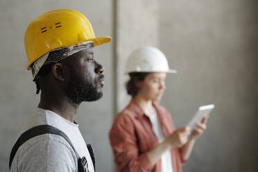 Construction worker wearing hardhat with coworker using tablet PC in background - DSHF01349