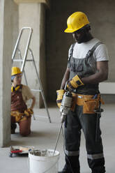 Bauarbeiter beim Mischen von Zement mit einem Werkzeug im Eimer auf der Baustelle - DSHF01360