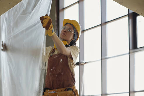 Junger Bauarbeiter, der auf der Baustelle Plastikfolie aufhängt - DSHF01362