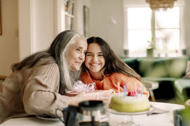 Smiling senior woman and granddaughter with birthday cake at home - MASF40588