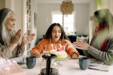 Cheerful girl celebrating birthday with mother and grandmother at home - MASF40589