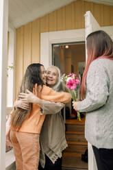 Cheerful senior woman welcoming daughter and granddaughter at house - MASF40603