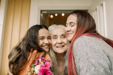 Cheerful senior woman greeting daughter and granddaughter in front of doorway - MASF40605