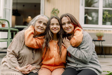 Portrait of smiling girl embracing mother and granddaughter on patio - MASF40642