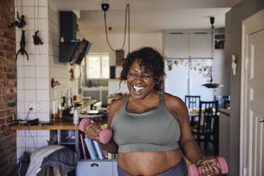 Joyful mature woman dancing and exercising with dumbbells at home - MASF40676