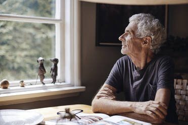 Contemplative senior man looking through window at home - MASF40688