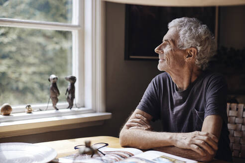 Contemplative senior man looking through window at home - MASF40688