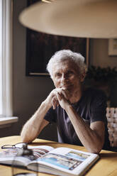 Porträt eines lächelnden älteren Mannes mit Hand am Kinn, der zu Hause sitzt - MASF40689