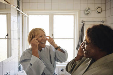 Happy multiracial female friends doing skincare together in bathroom at home - MASF40706