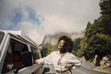 Lächelnde Frau mit geschlossenen Augen, die während einer Autoreise neben einem Van steht - MASF40716