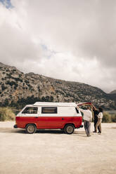 Male and female friends standing near van near mountains against sky - MASF40727