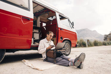 Ein junger Mann führt im Urlaub in der Nähe eines Lieferwagens fröhliche Videogespräche mit seinem Laptop - MASF40743