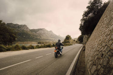 Man riding motorcycle on road in front of mountains aganist sky - MASF40747