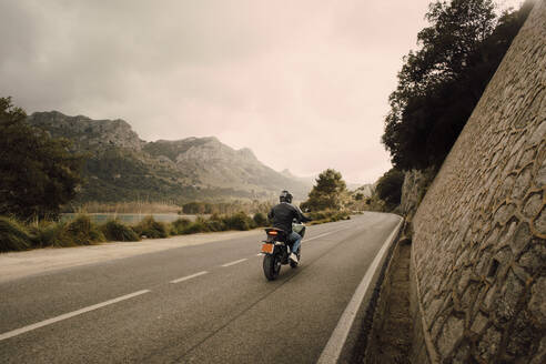 Ein Mann genießt eine malerische Motorradfahrt mit atemberaubender Aussicht auf die Berge und einen klaren blauen Himmel - MASF40747