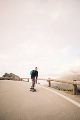 Young man skateboarding near wooden guardrail on road against sky - MASF40751