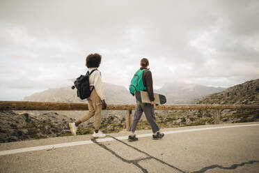 Young male and female friends looking at mountains while walking on road during vacation - MASF40758