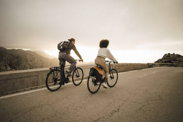 Male and female friends riding bicycles on road against sky - MASF40762