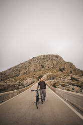 Ein junger Radfahrer bewundert die atemberaubende Berglandschaft, während er mit seinem Fahrrad auf einer Panoramastraße fährt - MASF40763