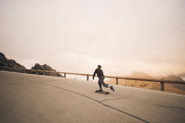 Young man skateboarding on road near railing against sky - MASF40775