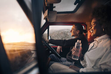Eine Frau lächelt, während ihr männlicher Freund auf ihrer vergnüglichen Autofahrt ein erfrischendes Getränk schlürft - MASF40779