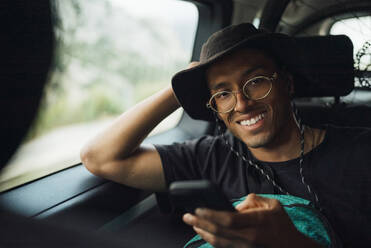 Portrait of happy man with smart phone sitting in van on vacation - MASF40795