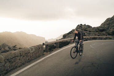 Ein junger Radfahrer genießt die atemberaubende Berglandschaft, während er auf der Straße fährt - MASF40802