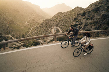 High angle view of male and female explorers cycling on road by mountains - MASF40808