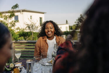 Eine Frau genießt eine köstliche Mahlzeit mit Freunden in der gemütlichen Atmosphäre ihres Hinterhofs und strahlt dabei pure Freude aus - MASF40873